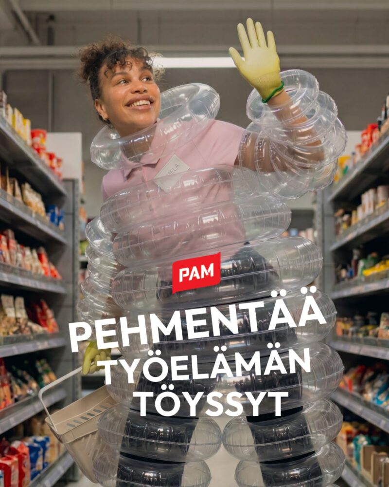 Hymyilevä nuori työntekijä vilkuttaa kaupan käytävällä. Häntä ympäröi uimarenkaat ja etualalla näkyy PAM-logo ja teksti "Pehmentää työelämän töyssyt".
