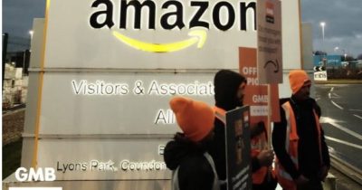 Amazonin logo ja työntekijöitä osoittamassa mieltään portilla
