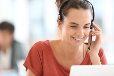 Hymyilevä nainen kuuloke korvalla vastaamassa asiointipalveluun tulleeseen puheluun.