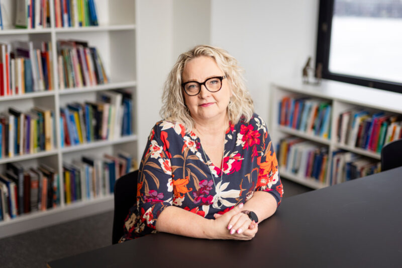 Työympäristöasiantuntija Erika Kähärä istuu pöydän ääressä ja hymyilee kameralle.