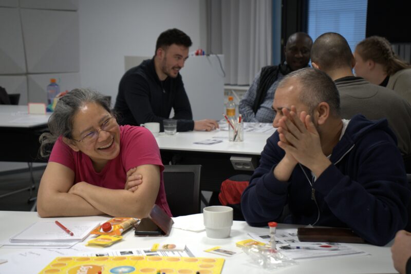 A woman and a man are laughing while playing a game. Other people playing in background.
