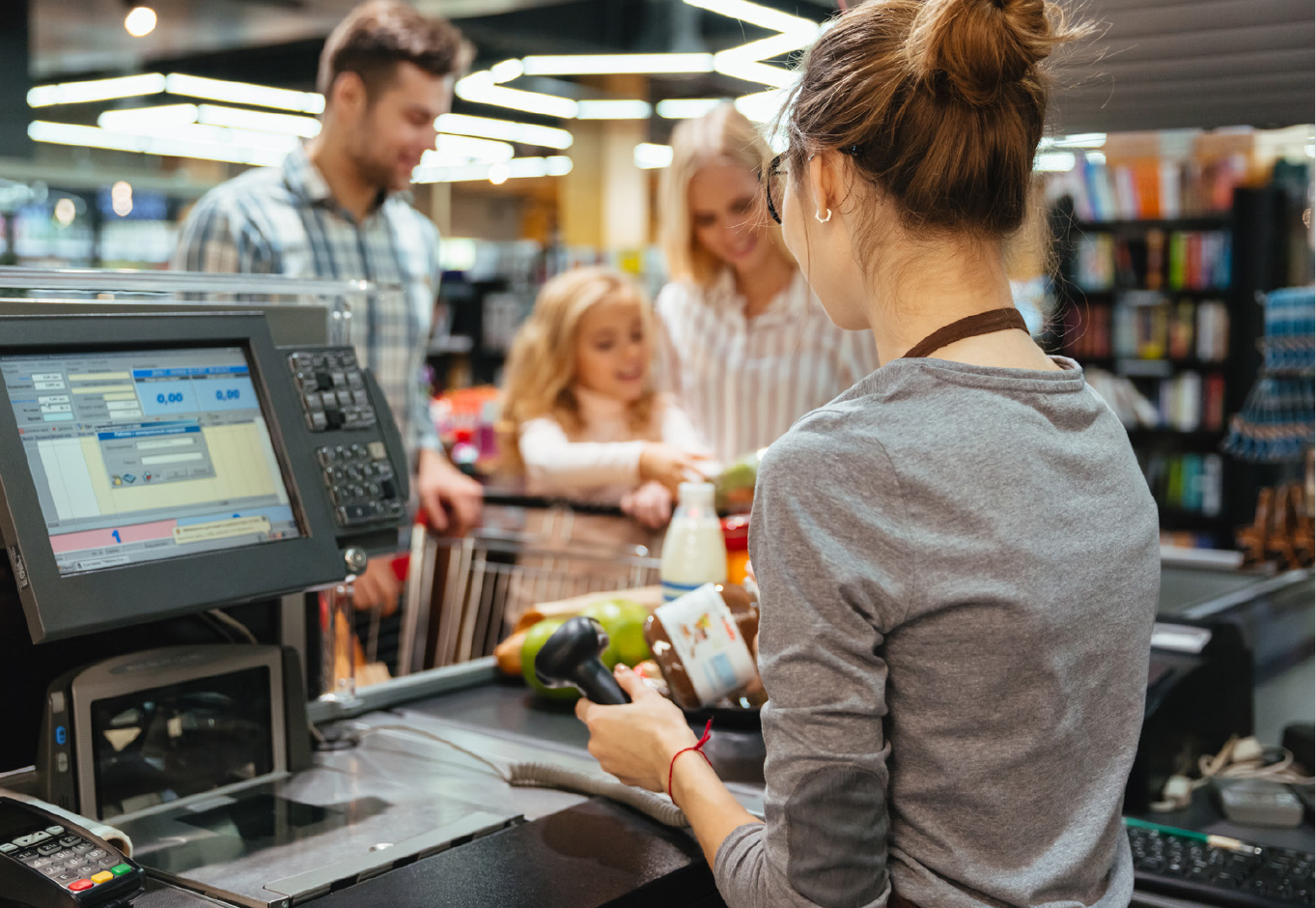 Päivitetystä oppaasta poimittu kuvituskuva, jossa työntekijä piippaa tuotteita kaupan kassalla. Taustalla perhe.