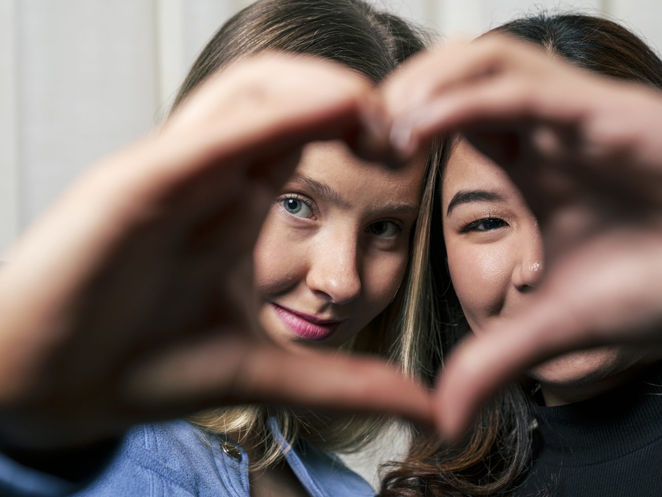 Kaksi nuorta näkyvät taustalla. Yhdessä he muodostavat käsillään  sydämen kasvojensa eteen.