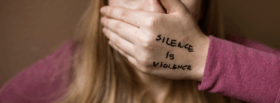Nainen peittää suunsa kädellään. Kädessä lukee "silence is violence".