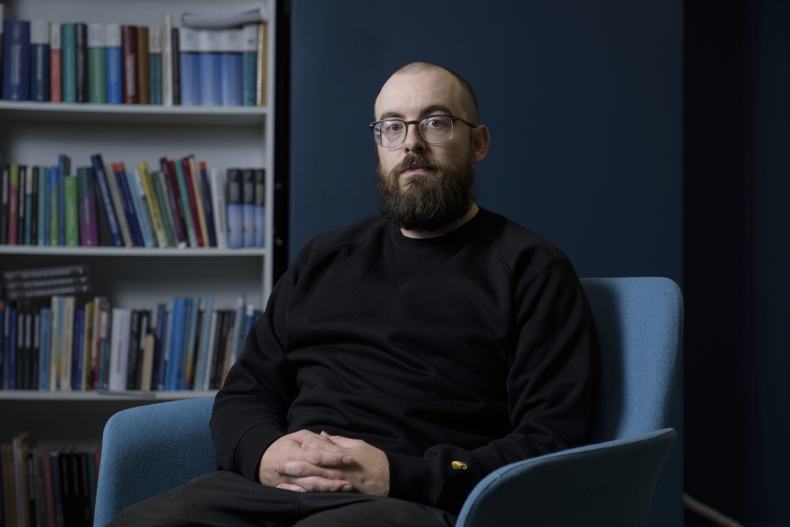 Fred Miller, Chair of PAM’s Impact Forum, sitting with a serious expression, a blurred bookshelf in the background.