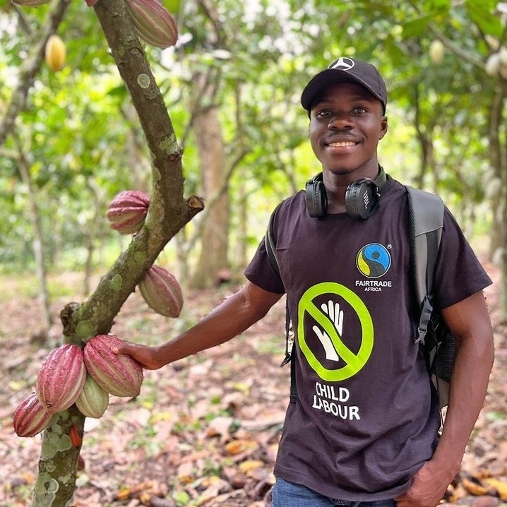 Ghanalainen kaakaonviljelija seisoo kaakaopuun edessä.