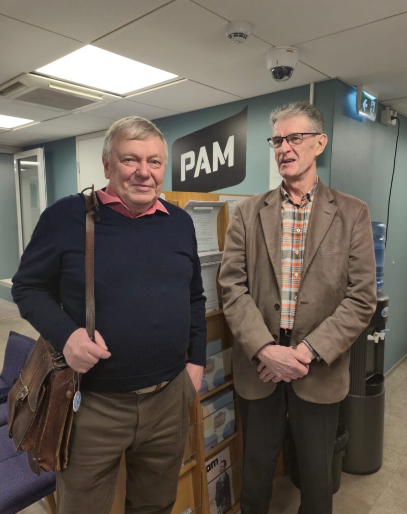 kaksi miestä PAMin logon edessä