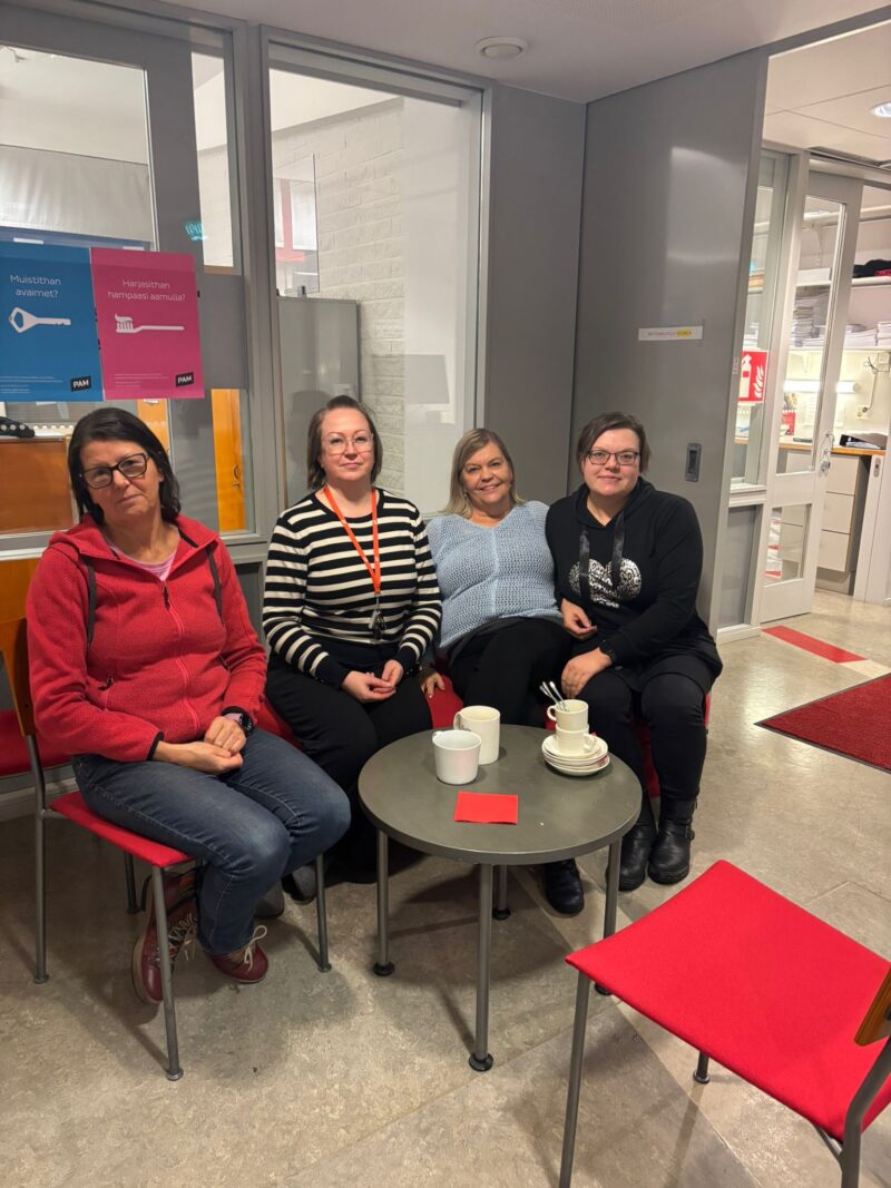 neljä ihmistä istuu PAin toimistolla kakkukahveilla