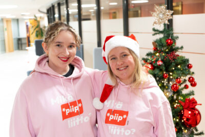 Kuvassa kaksi vaaleahiuksista nuorta naista vaaleanpunaiset hupparit päällä, joissa lukee mikä *piip* liitto ja taustalla joulukuusi.