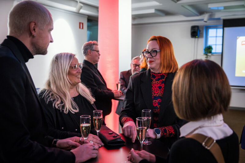 Ihmisiä öydän ympärillä kuohuviinilasit kädessä