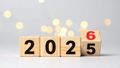Wooden block cubes on a light grey surface read "2025" while the last cube is being flipped to show a red "6" — visual symbol for the shift to 2026 and changes in the new year.