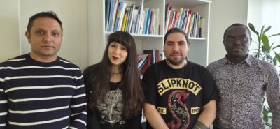 Four new workplace representatives standing side by side in an office in front of a bookshelf, smiling and looking confident and united.