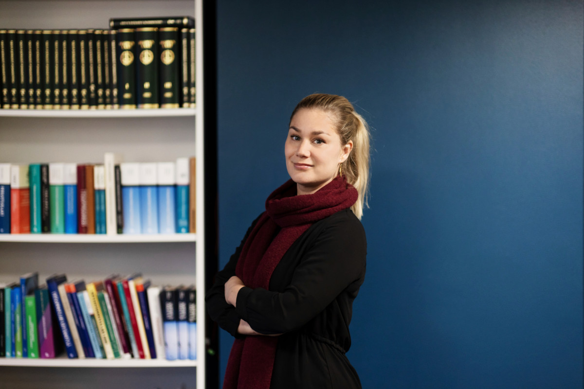 PAMin juristi Sanna Kyröläinen seisoo käsivarret puuskassa ja hymyilee taustallaan kirjahylly ja tummansininen seinä.
