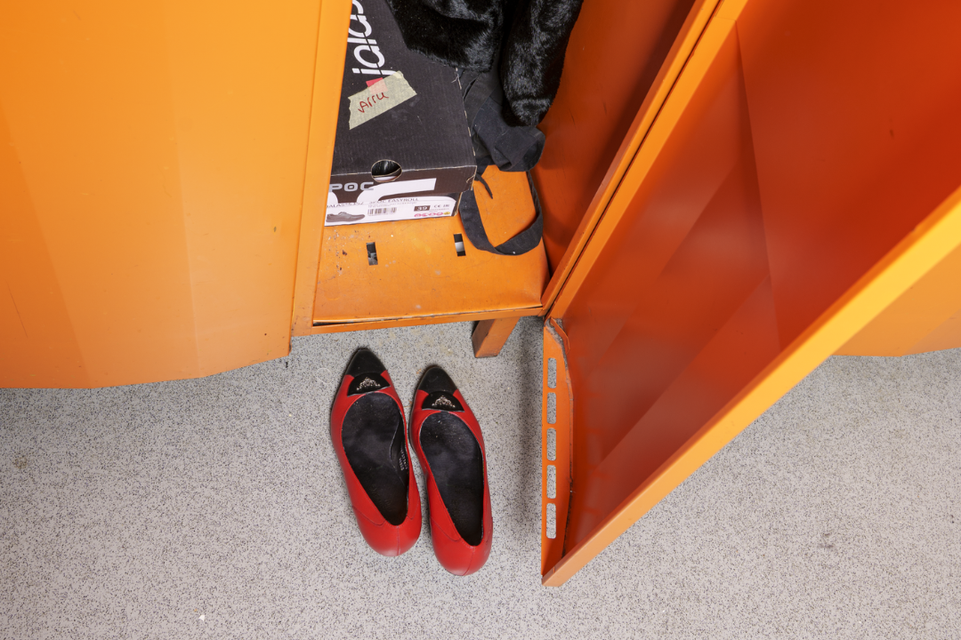 Avoin oranssi kaappi, sen edessä lattialla punaiset avokkaat ja kaapissa näkyvä laukku sekä takki.