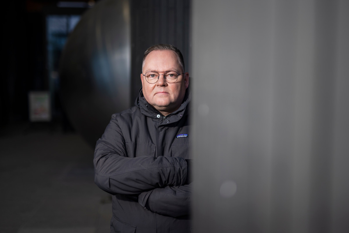 Kuvassa PAMin järjestöjohtaja Risto Kalliorinne kädet puuskassa ja katse suoraan kameraan, seisoo hämärässä aulatilassa seinän vieressä; ilme vakaa ja päättäväinen.