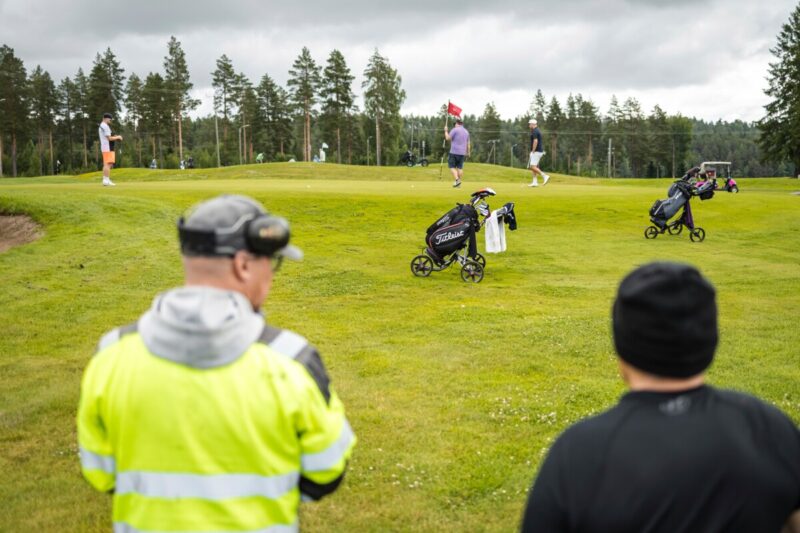 Kaksi miestä katselevat pelaajia Siilinjärven Tarinagolfin kentällä.